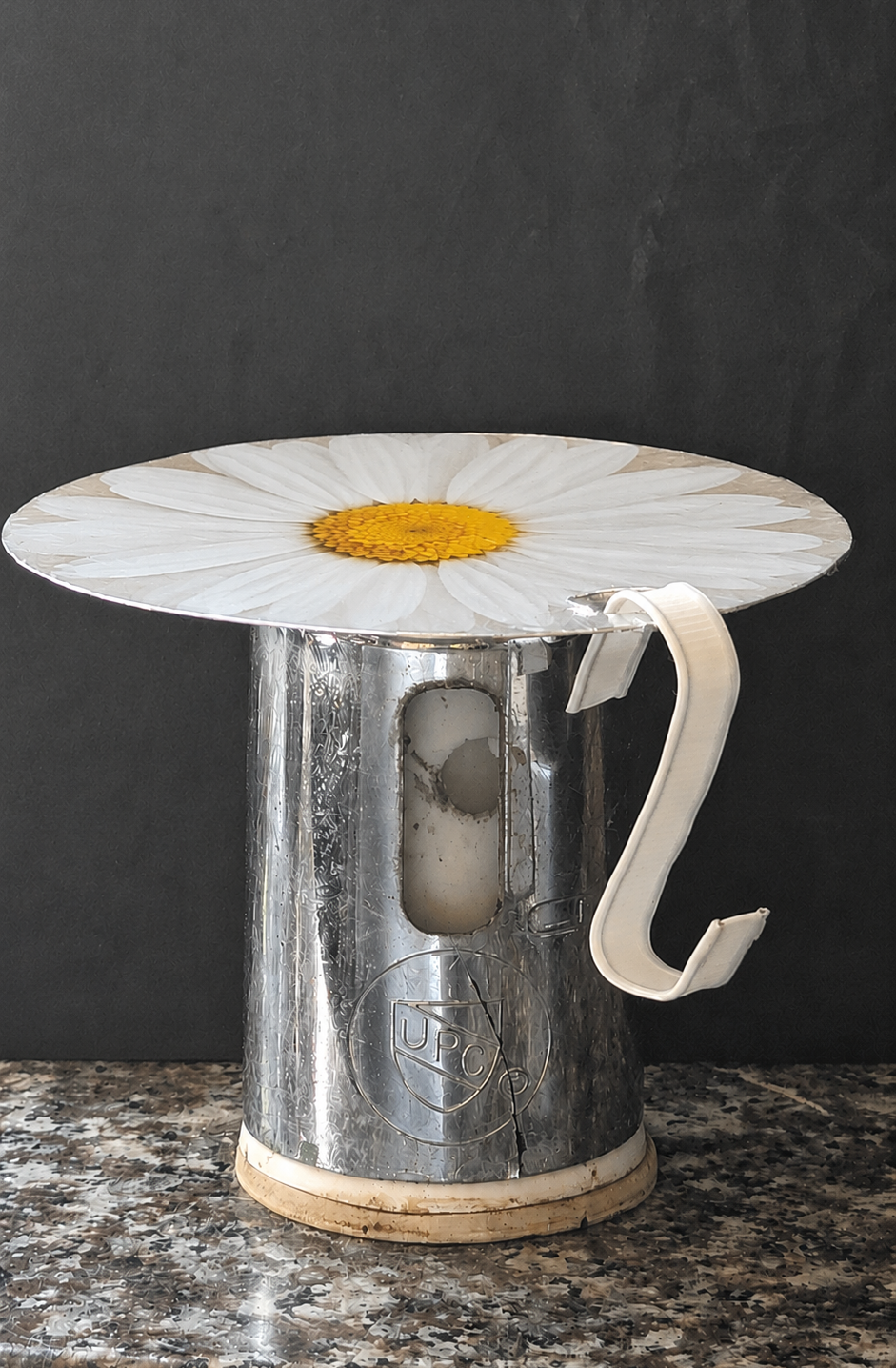 The stand prototype: a chromed cylindrical base with a wide disc top and a side hook, shown against a slate background
